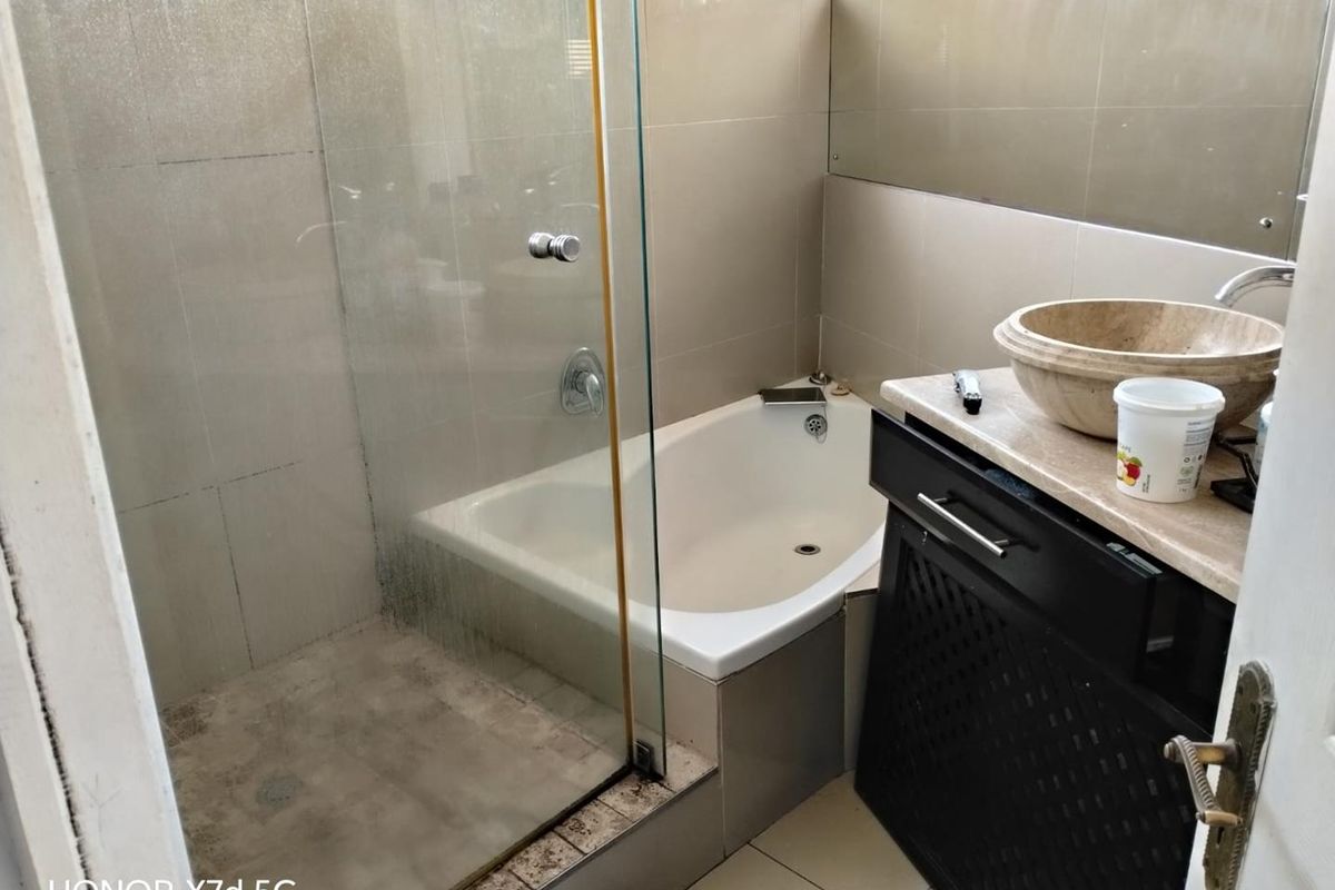 Compact bathroom featuring a built-in bathtub, glass-enclosed shower, and a stone vessel sink set on a dark vanity cabinet.