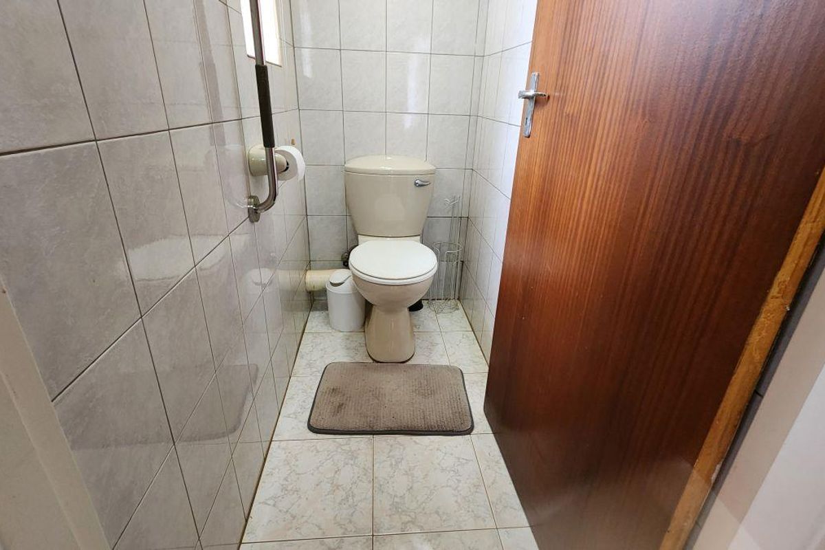 A compact guest toilet featuring full-height wall tiling, a standard ceramic toilet, and a wooden door.