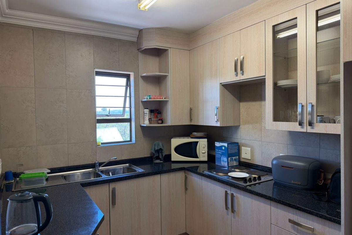 A functional kitchen featuring light wood-finish cabinetry, dark granite countertops, a double basin sink, and a built-in electric hob with tiled splashbacks.