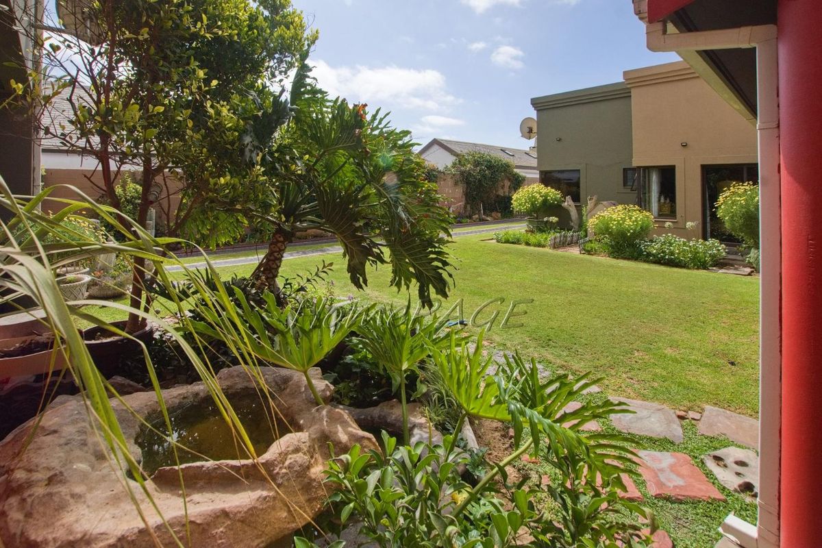 A well-maintained rear garden featuring a manicured lawn, established landscaping, and a decorative stone water feature.