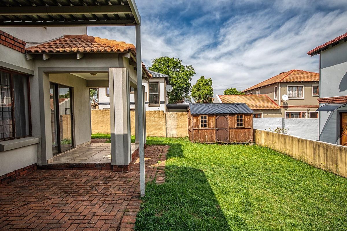 A private rear garden featuring a covered patio with brick paving, a lawn area, and a detached wooden storage shed.
