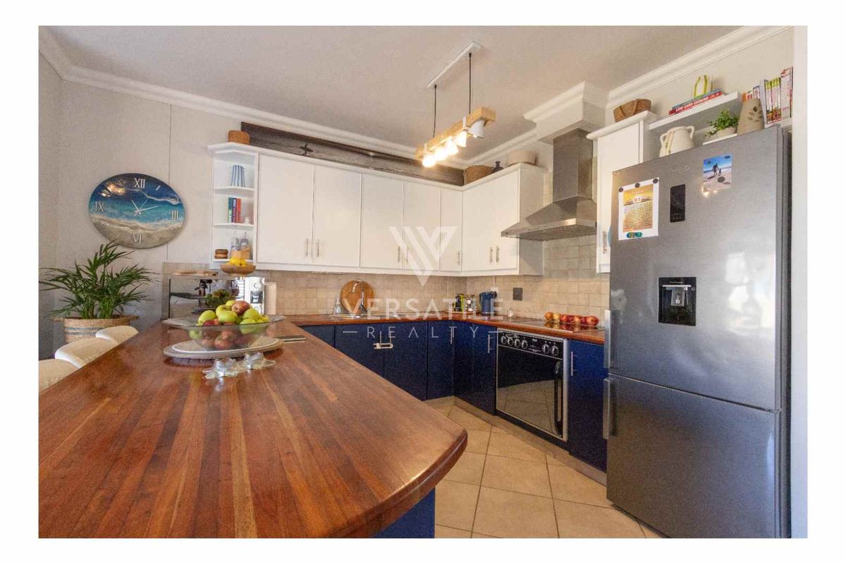 Modern kitchen featuring two-tone cabinetry, a wooden breakfast bar, stainless steel extractor fan, and tiled flooring.
