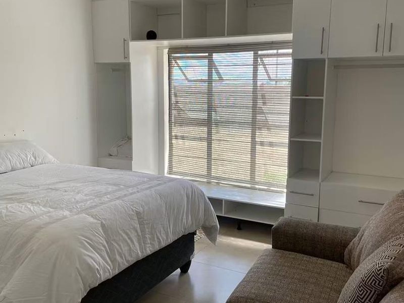 A well-lit bedroom featuring extensive white built-in cabinetry surrounding a window with blinds and neutral tiled flooring.