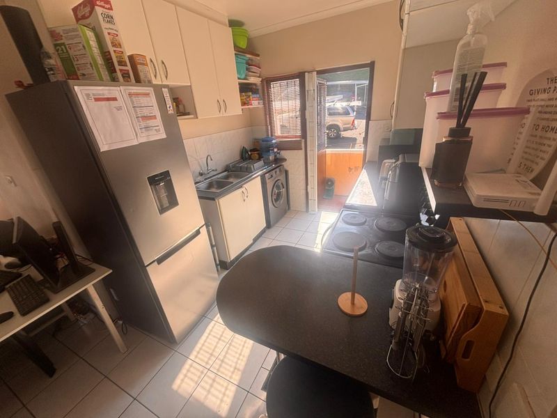Compact kitchen featuring built-in cabinetry, tiled flooring, electric hob, and direct access to the exterior.