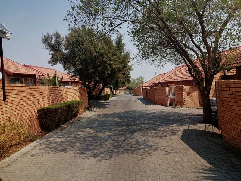 A view of the paved driveway and street within the residential cluster complex, featuring face brick boundary walls and tiled roof units.