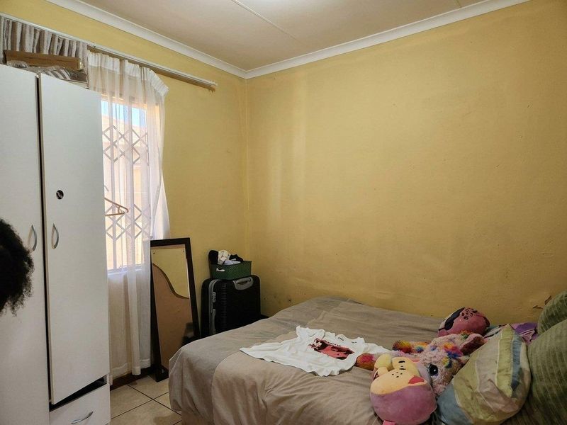 A bedroom featuring tiled flooring, a window with a security gate, and cove cornicing, requiring cosmetic updates to the wall finishes.