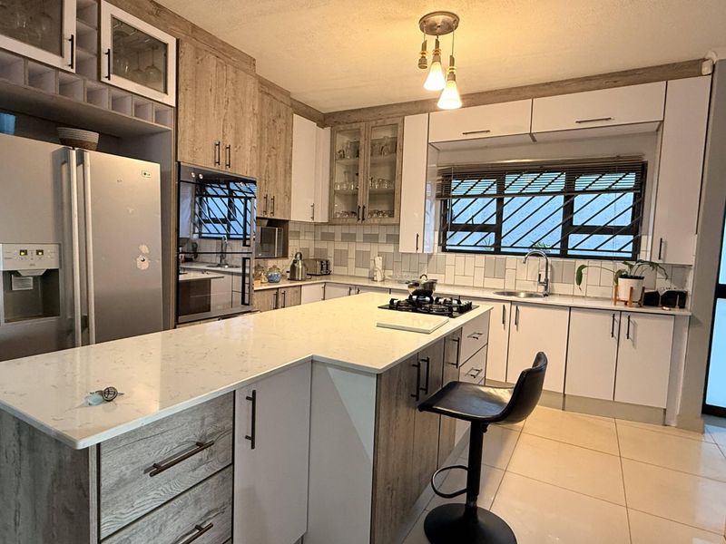 Modern kitchen featuring a central island with quartz countertops, gas hob, built-in oven, and ample cabinetry with a neutral tiled backsplash.