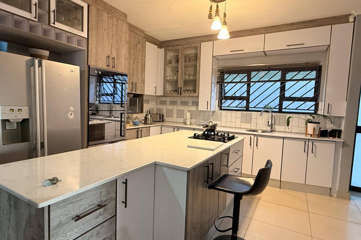 Modern kitchen featuring a central island with quartz countertops, gas hob, built-in oven, and ample cabinetry with a neutral tiled backsplash.