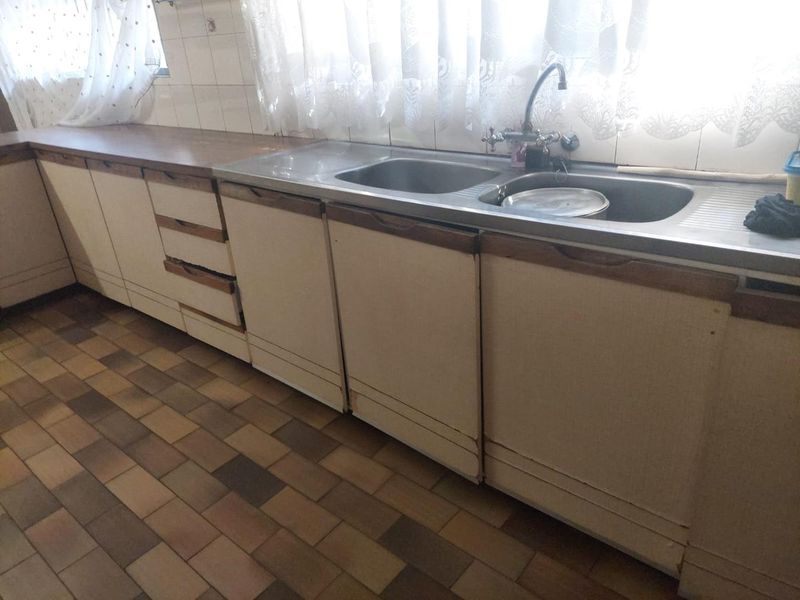 A dated kitchen featuring a double bowl stainless steel sink, laminate countertops, and tiled flooring, offering significant potential for a modern renovation.