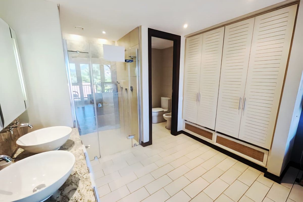 Spacious bathroom featuring dual vessel sinks on a stone vanity, a glass-enclosed walk-in shower, and extensive built-in cabinetry for storage.