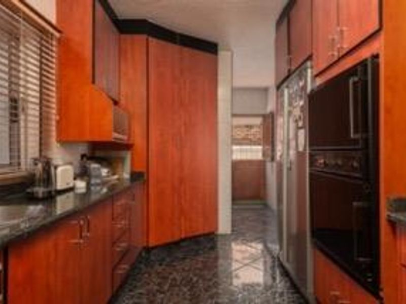 A functional kitchen featuring warm-toned wooden cabinetry, dark granite countertops, and a built-in double wall oven with tiled flooring.
