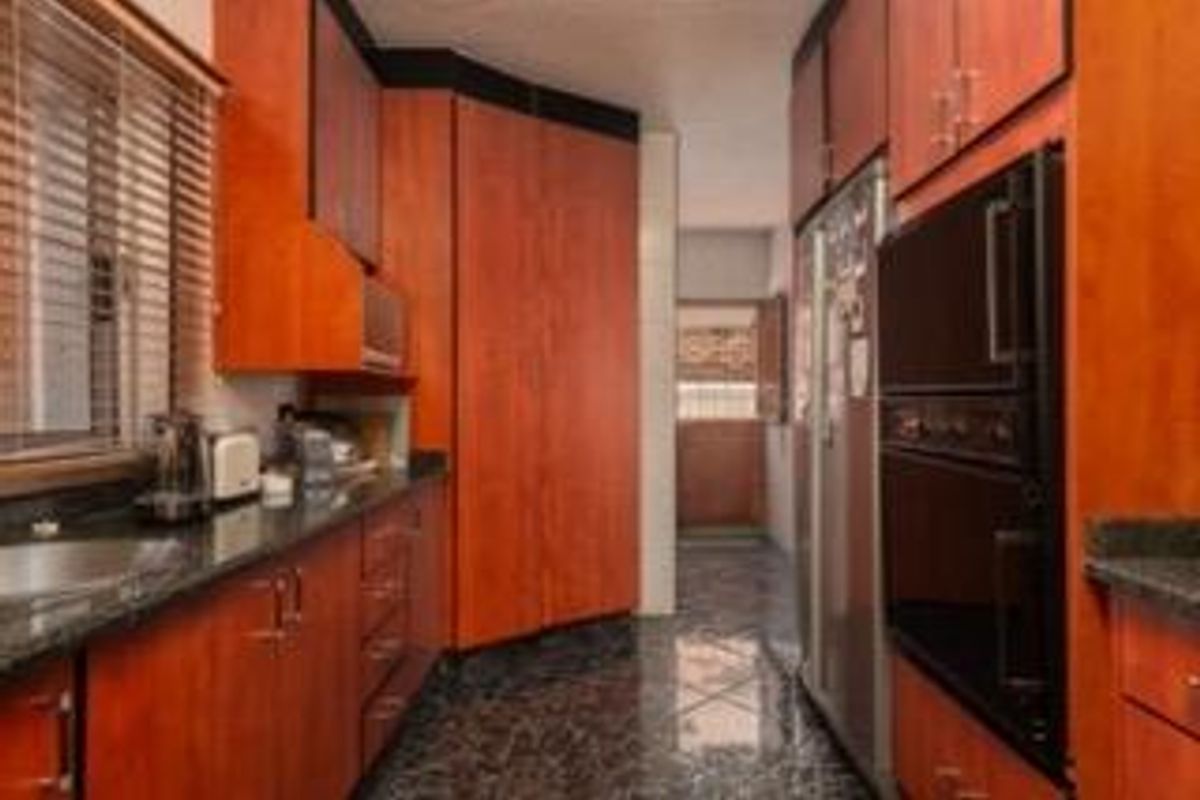 A functional kitchen featuring warm-toned wooden cabinetry, dark granite countertops, and a built-in double wall oven with tiled flooring.
