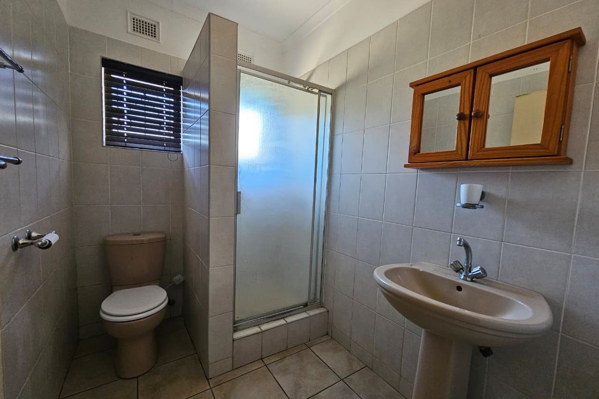 A functional bathroom featuring a tiled shower enclosure, pedestal basin, and toilet, finished with neutral wall and floor tiles.