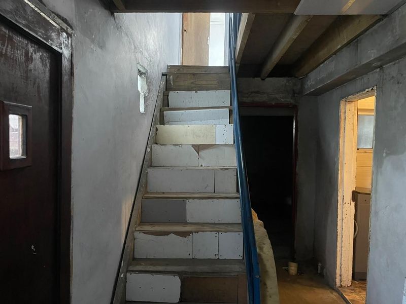 A hallway area featuring an unfinished staircase with exposed structural elements and incomplete wall plastering, requiring significant renovation and finishing work.