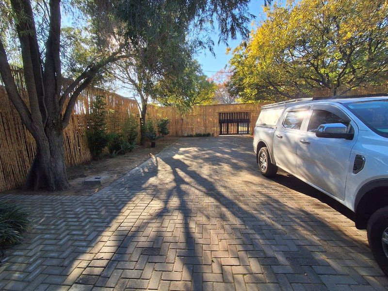 A paved driveway leading to a secure gated entrance, enclosed by bamboo fencing and mature trees.