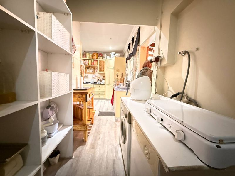 A functional scullery and laundry area featuring built-in shelving, cabinetry, and plumbing connections for laundry appliances, providing practical utility space.