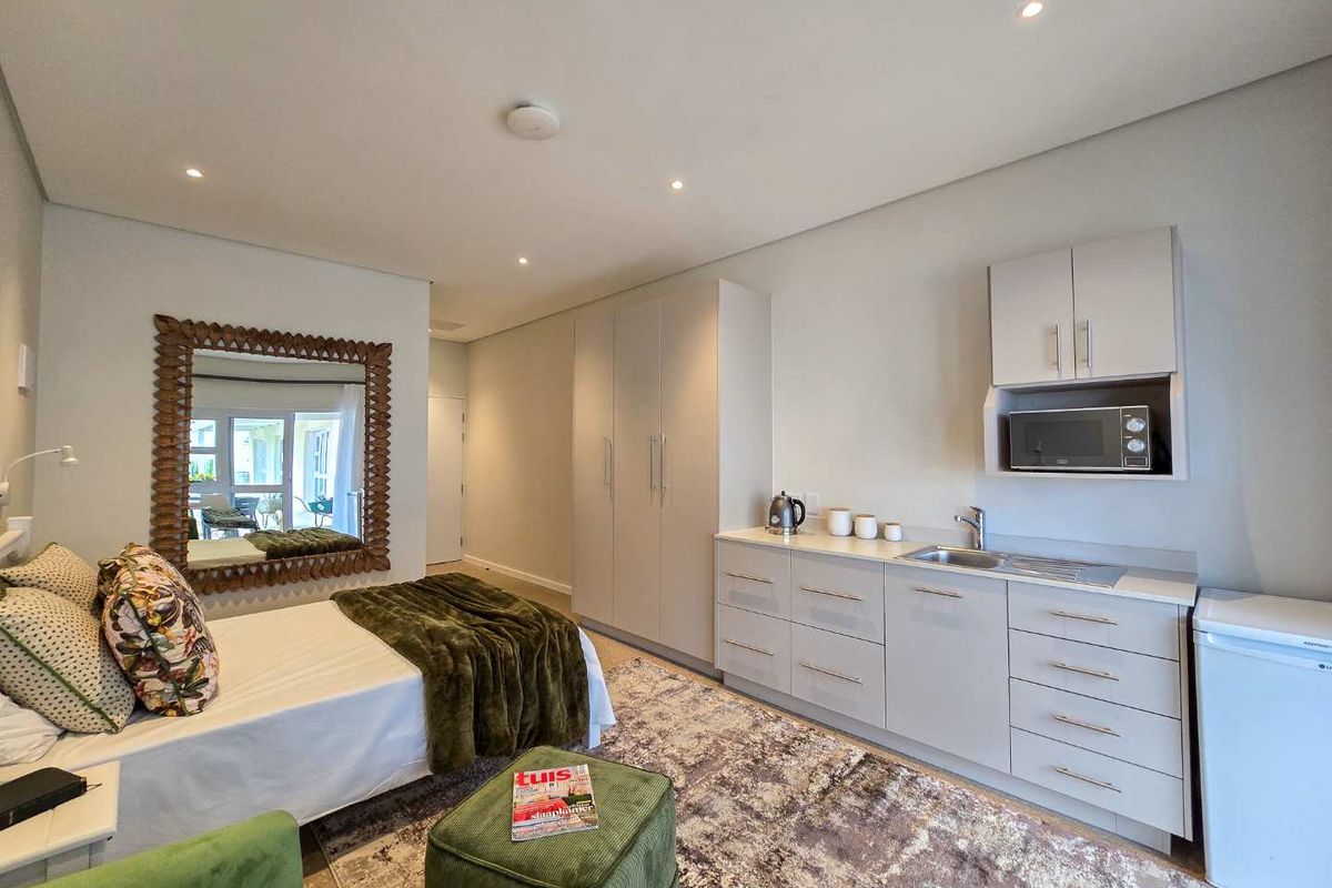 A well-appointed studio bedroom featuring built-in cabinetry, a compact kitchenette with sink and microwave, and recessed ceiling lighting.