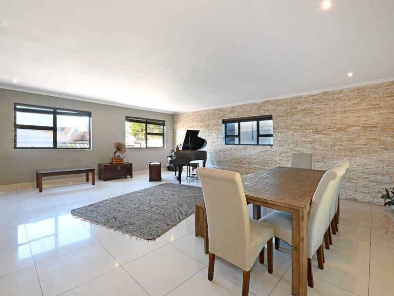 Spacious open-plan living and dining area featuring polished tile flooring, a textured stacked stone feature wall, and ample natural light through aluminium-framed windows.