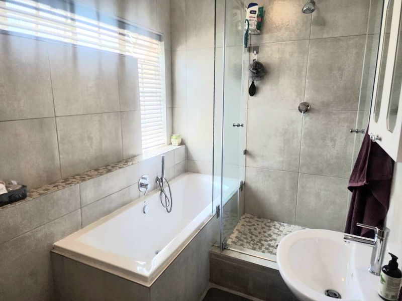 Modern bathroom featuring a built-in bathtub, separate glass-enclosed shower, and neutral tiled finishes throughout.