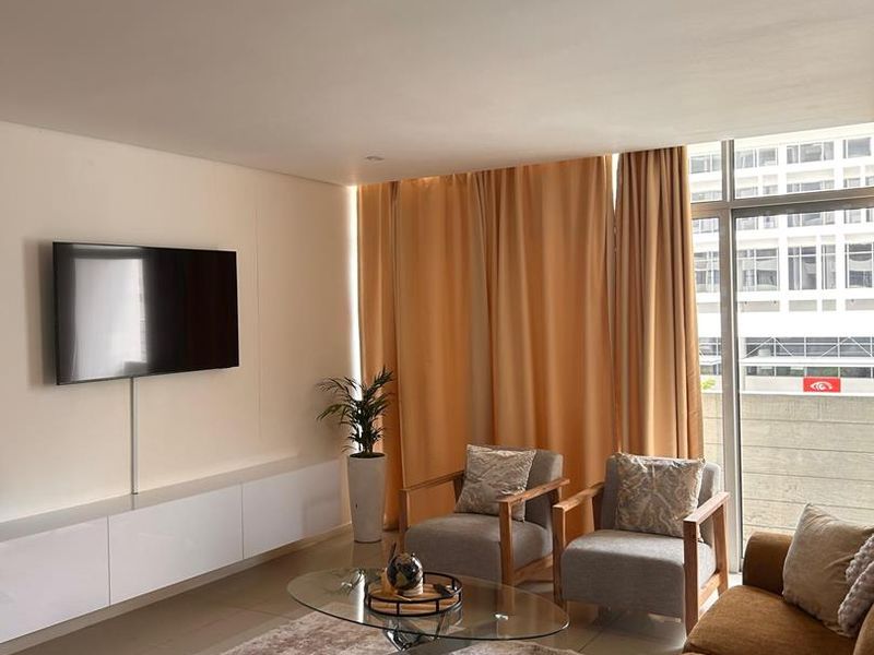 A bright living room featuring tiled flooring, a built-in media console, and a large sliding glass door providing natural light and balcony access.