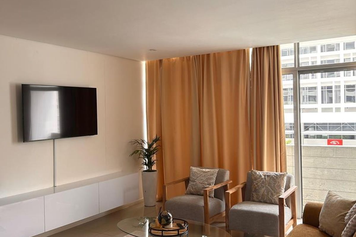 A bright living room featuring tiled flooring, a built-in media console, and a large sliding glass door providing natural light and balcony access.