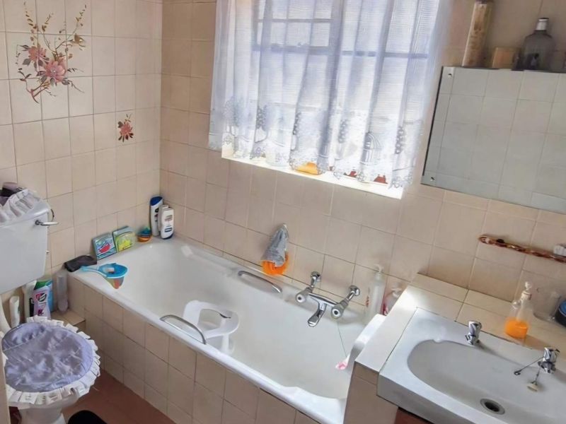 A functional bathroom featuring a built-in bathtub, wall-mounted basin, and ceramic wall tiling. The space is dated and would benefit from modern updates.
