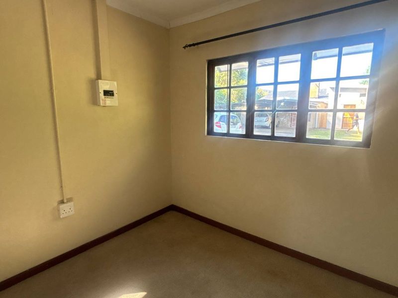 An empty bedroom featuring a multi-pane window, carpeted flooring, and exposed electrical conduit, offering a blank canvas for renovation or restyling.
