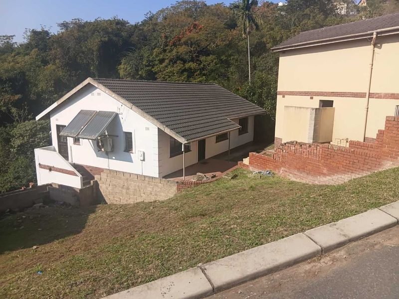Rear view of the property featuring a tiled roof, solar water heating system, and a paved patio area with surrounding brick retaining walls.