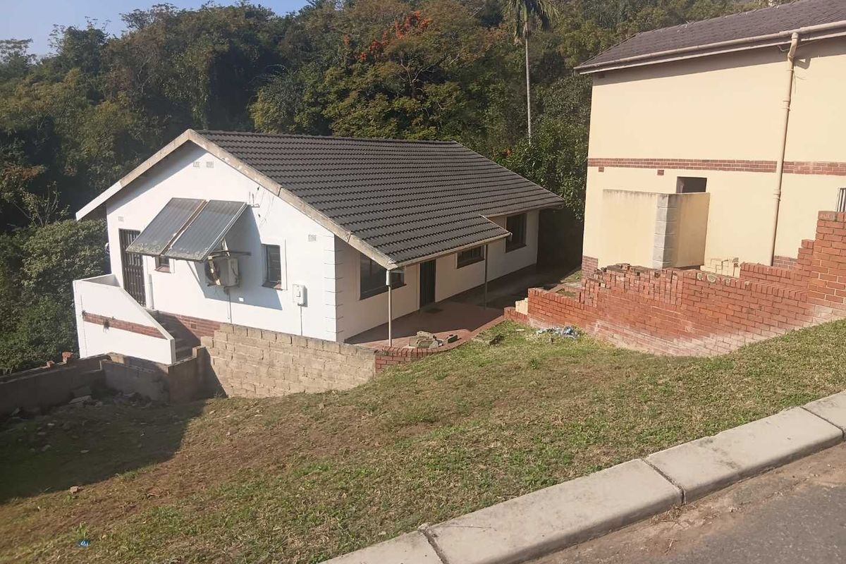 Rear view of the property featuring a tiled roof, solar water heating system, and a paved patio area with surrounding brick retaining walls.
