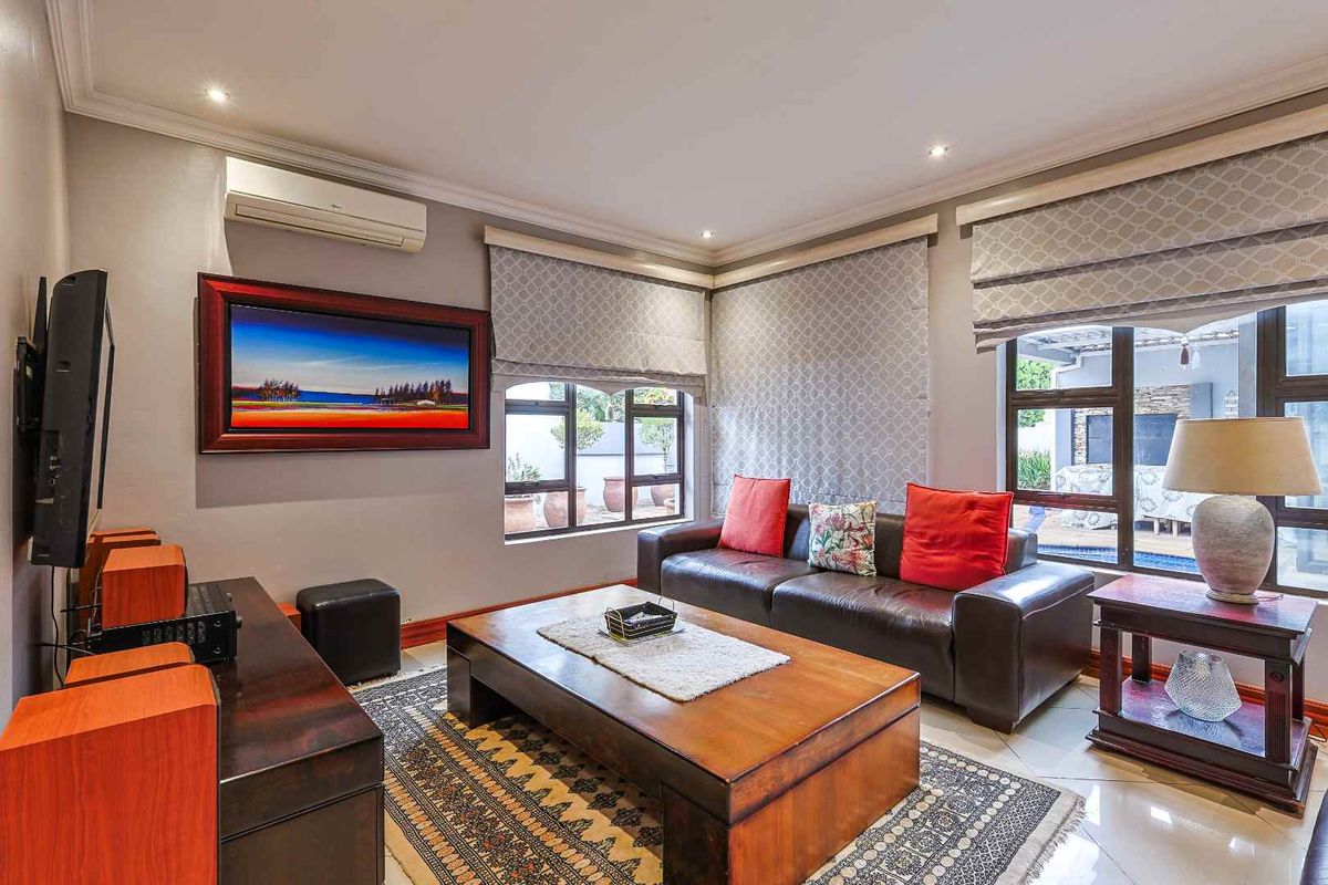 A well-maintained living room featuring tiled flooring, recessed downlighting, and a wall-mounted air conditioning unit, with large windows providing natural light.