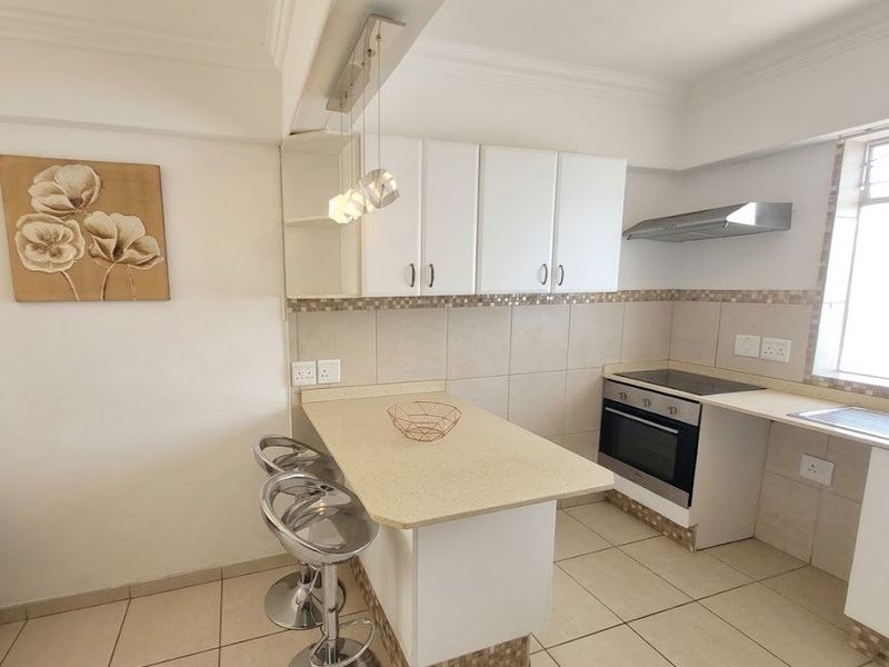A functional kitchen featuring white cabinetry, stone countertops, a breakfast bar, and integrated appliances including an oven, hob, and extractor fan.