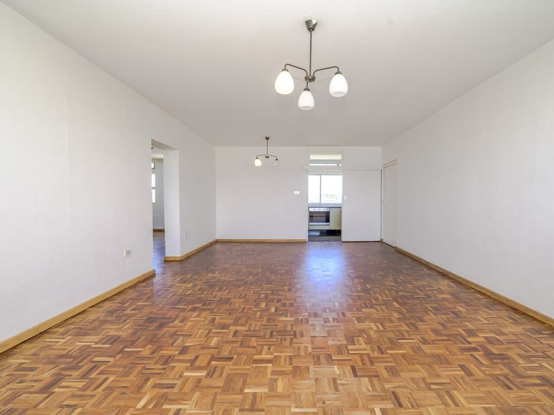 A spacious, empty living area featuring traditional parquet flooring and neutral walls, offering a versatile blank canvas for interior design.