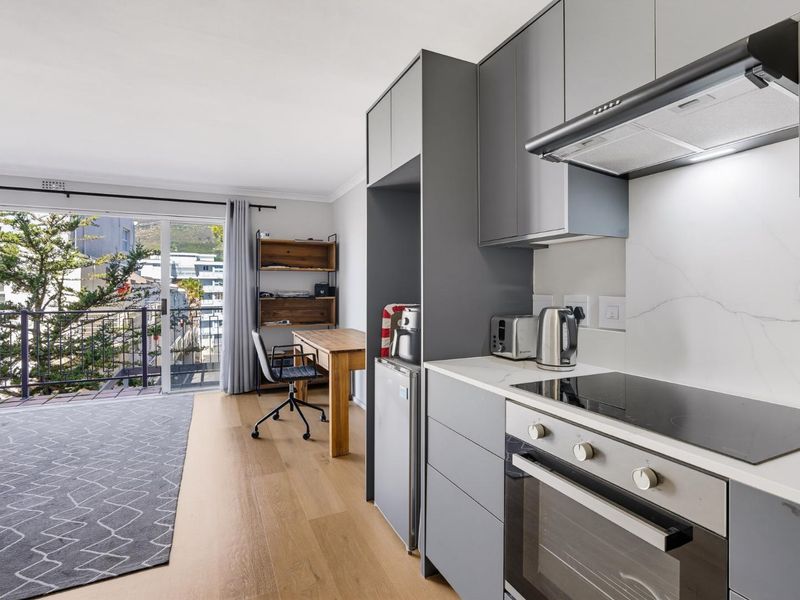 Modern open-plan kitchen and living area featuring sleek grey cabinetry, integrated appliances, and a sliding door leading to a private balcony with urban views.