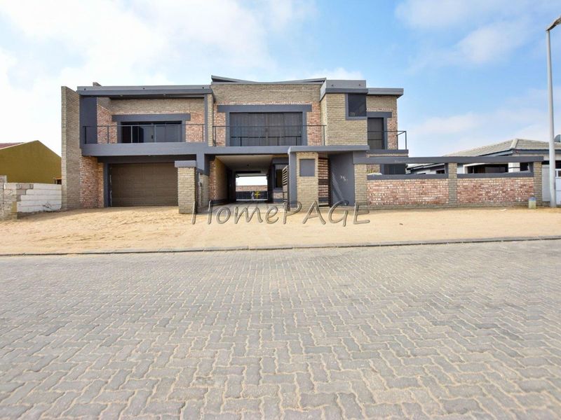 Modern double-story brick residence featuring a double garage, upper-level balcony, and a paved street-facing approach.