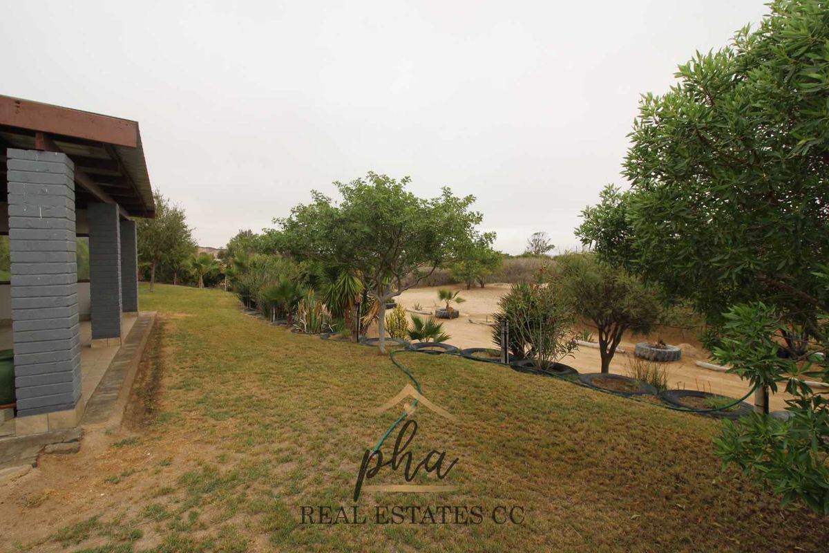 View of the rear garden area featuring a covered patio structure and established landscaping on the small holding.