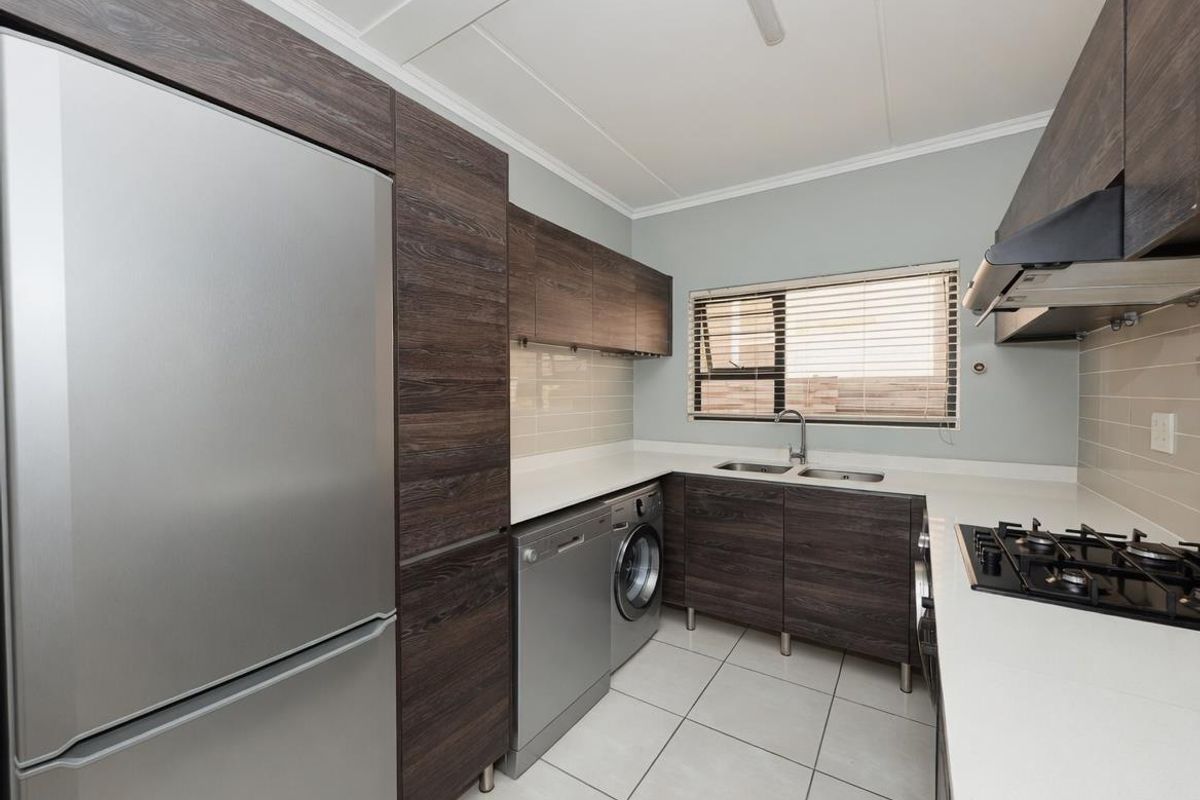 Modern kitchen featuring dark wood-grain cabinetry, stone countertops, gas hob with extractor, and integrated space for laundry appliances.
