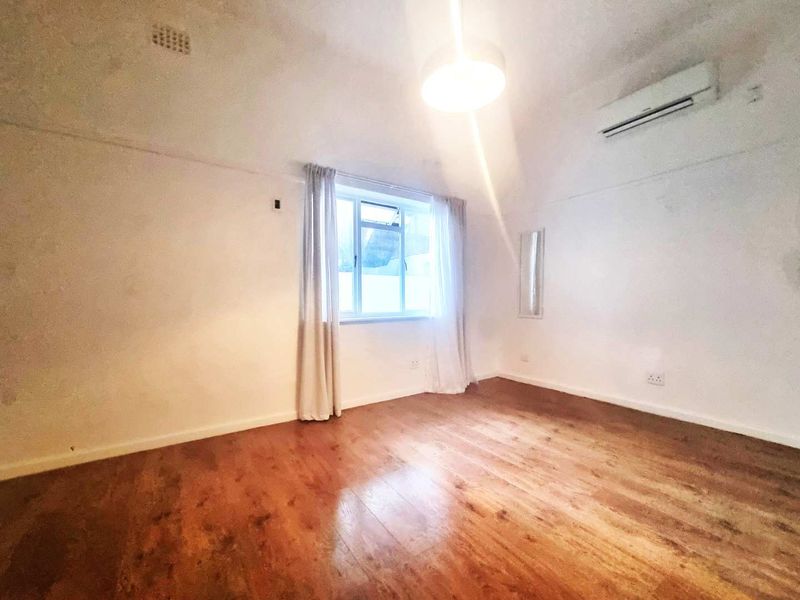 A bright, empty bedroom featuring laminate flooring, a wall-mounted split-system air conditioner, and a central ceiling light fixture.