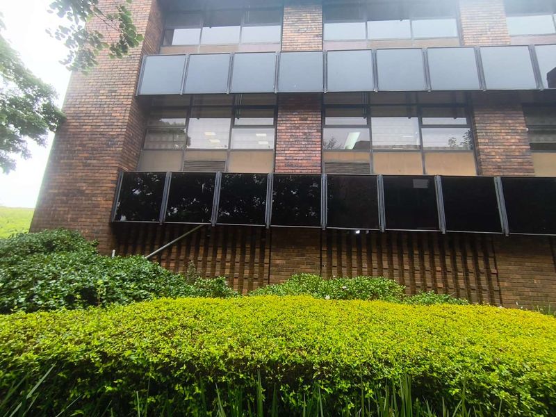 A view of the office building exterior featuring a classic brick facade, large tinted windows, and well-maintained garden landscaping.