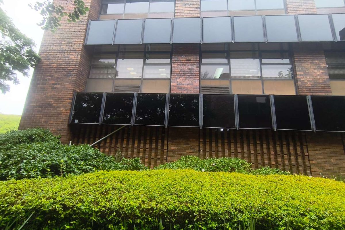 A view of the office building exterior featuring a classic brick facade, large tinted windows, and well-maintained garden landscaping.