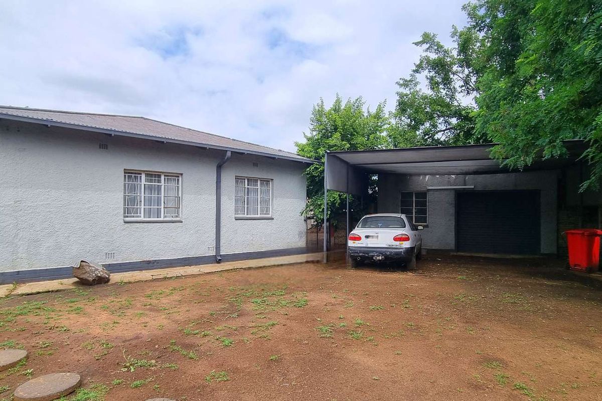 Exterior view of the house featuring a covered carport, metal window frames, and a spacious yard area.
