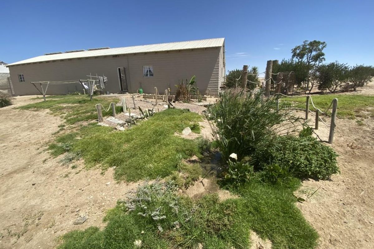 A view of the rear exterior of the property featuring a large yard with natural landscaping and a simple building structure.