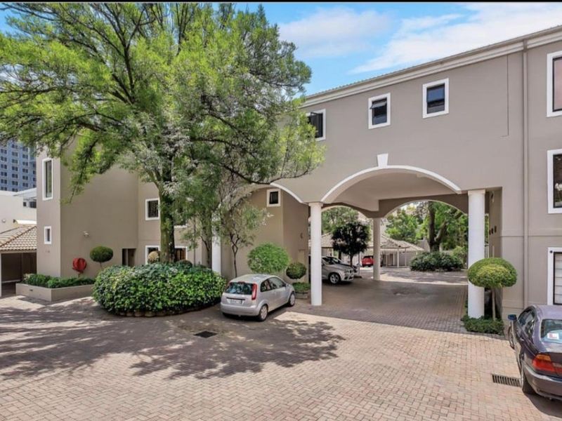 Front elevation of the apartment complex featuring a paved driveway, covered archway entrance, and well-maintained landscaped garden areas.
