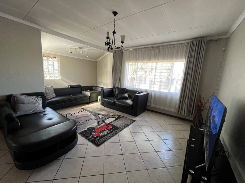 A spacious living room featuring tiled flooring, a large window with curtain tracks, and a glass block accent window.