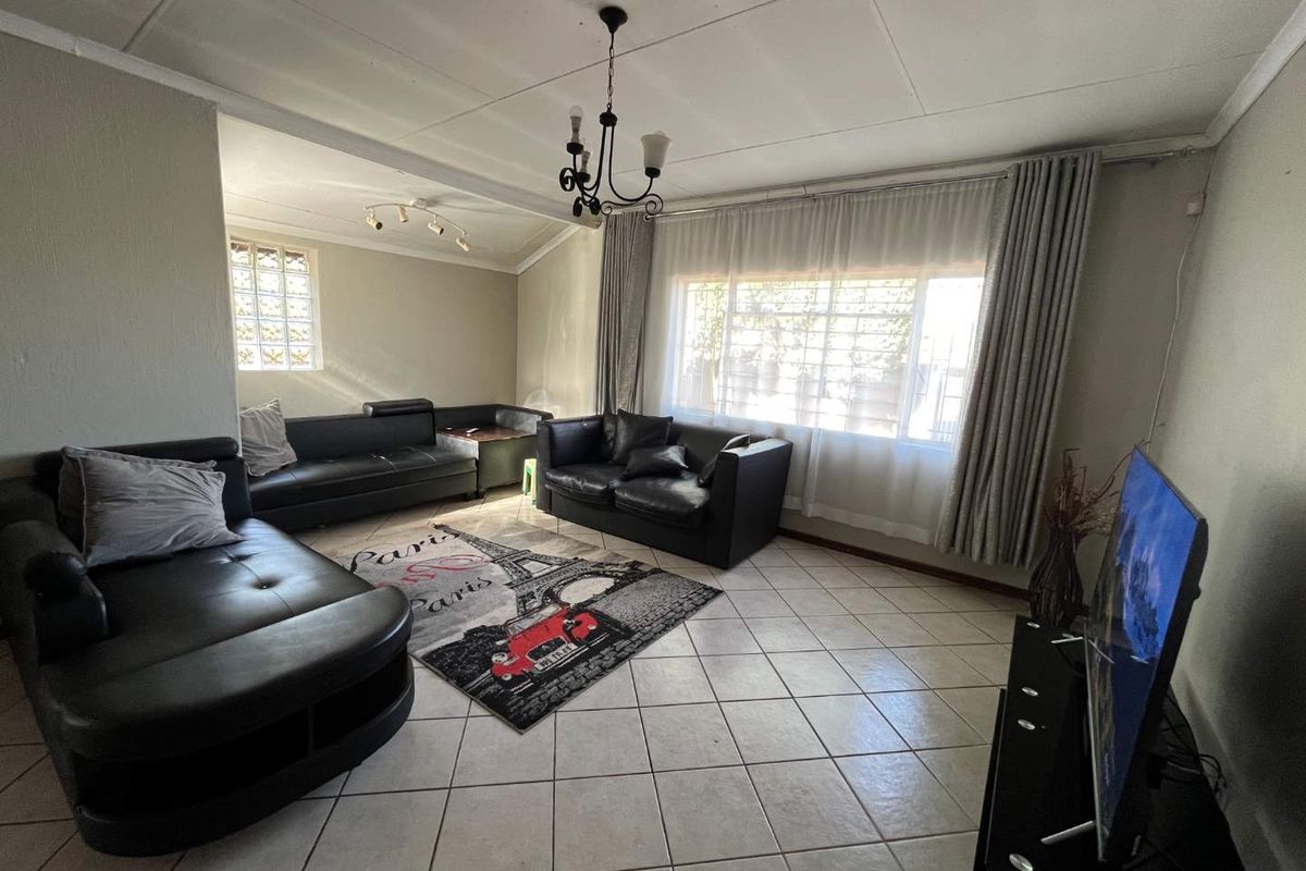A spacious living room featuring tiled flooring, a large window with curtain tracks, and a glass block accent window.