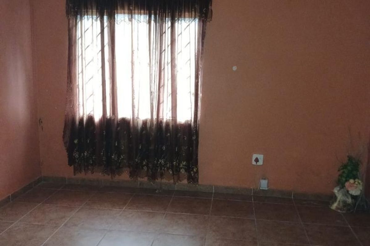 An empty living room featuring brown tiled flooring and terracotta-toned walls, providing a blank canvas for potential interior design updates.