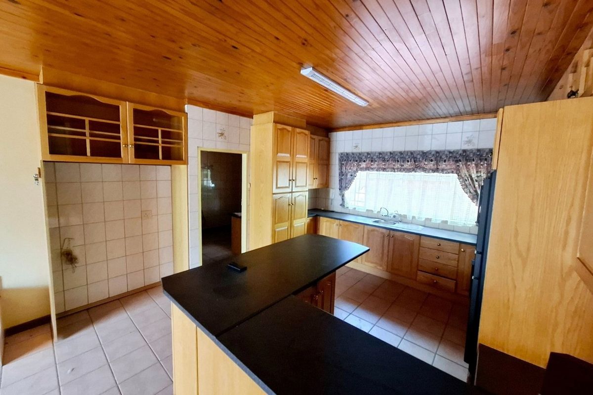A spacious kitchen featuring wooden cabinetry, dark laminate countertops, tiled splashbacks, and a distinctive wooden tongue and groove ceiling.