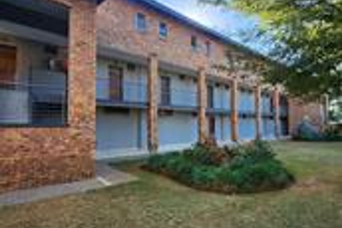 Exterior view of a multi-story apartment building featuring face brick construction, private balconies with metal railings, and a landscaped garden area.