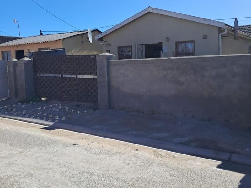 Front exterior view of a single-story house featuring a perimeter wall, metal gate, and security entrance gate.