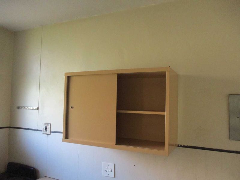 A basic kitchen area featuring a wall-mounted metal storage cabinet, electrical outlets, and a tiled splashback, requiring cosmetic updates.