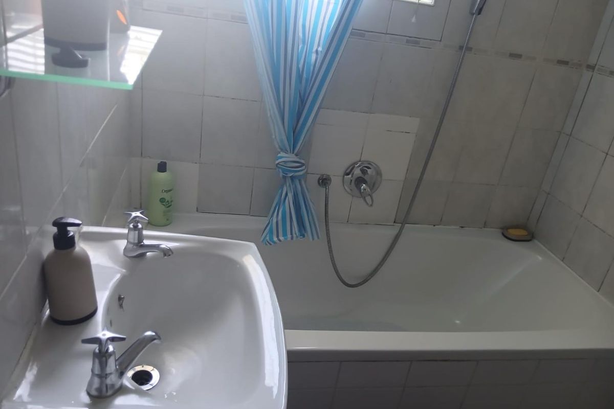 A functional bathroom featuring a white pedestal basin and a bathtub with a handheld shower mixer, finished with wall tiling.